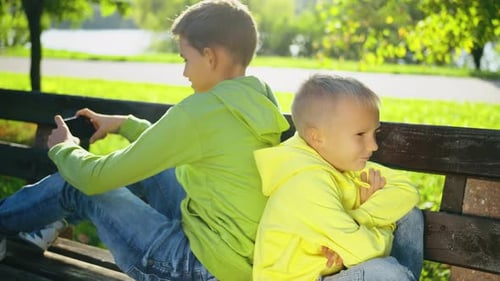 El hermano menor se molesta mientras el hermano mayor usa un teléfono inteligente