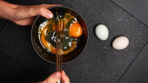 Eier in einer Schüssel mit verschiedenen Farben auf einer dunklen Küchenoberfläche vermischen.