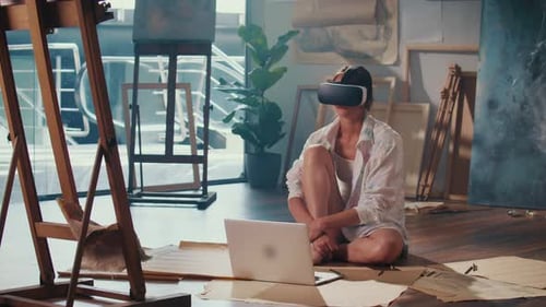 A Female Artist Using VR Headset to Paint in His Bright Studio Surrounded By Artwork