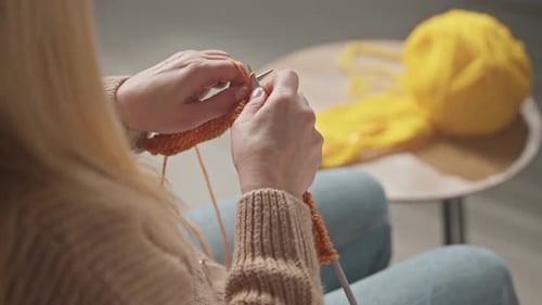Woman Knitting with Knitting Needles and Orange Yarn