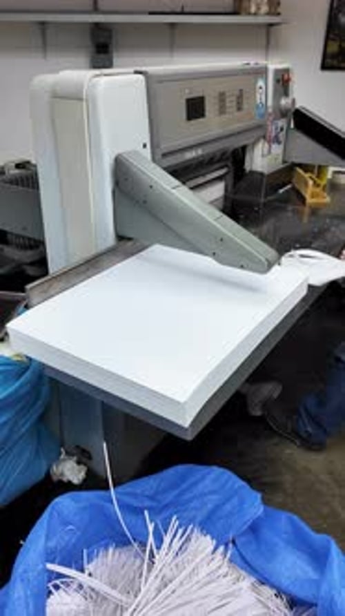 Large industrial paper cutting Polar, with stack of white paper being processed by a man