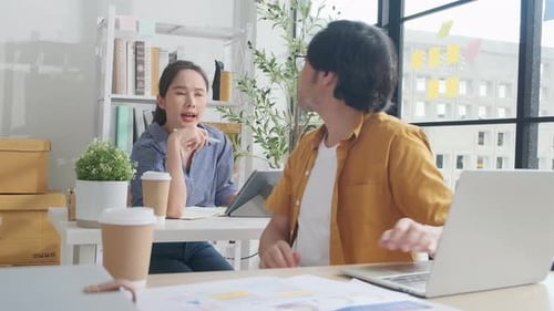 Two young Asian startup partners are working in a casual small business office.