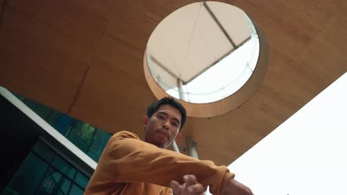 Hispanischer Tänzer schaut in die Kamera, während er am Wolkenkratzer tanzt. Hip-Hop.