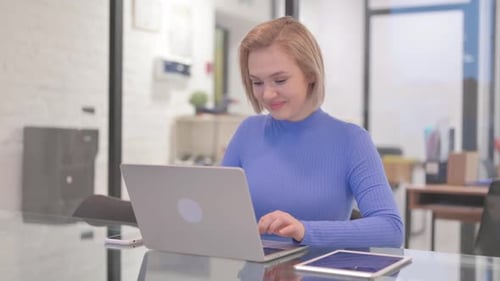 Young Woman Smiling at Camera while Working on Laptop in Office