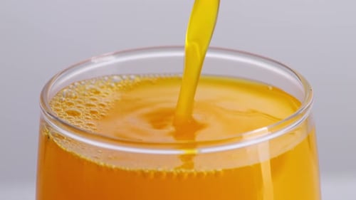 Close Up Of Orange Juice Being Poured Into A Glass On The Light White Screen Background