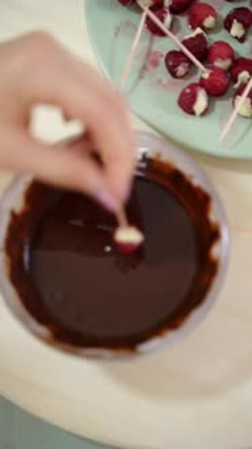 Woman Dips Raspberry on Skewer in Chocolate Bowl
