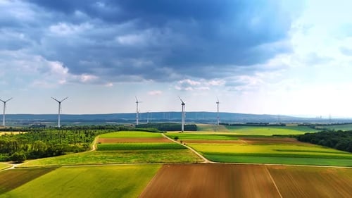 Picturesque fields under the rainy cloudscape. Lots of wind mills rotate in the wind. Aerial view.