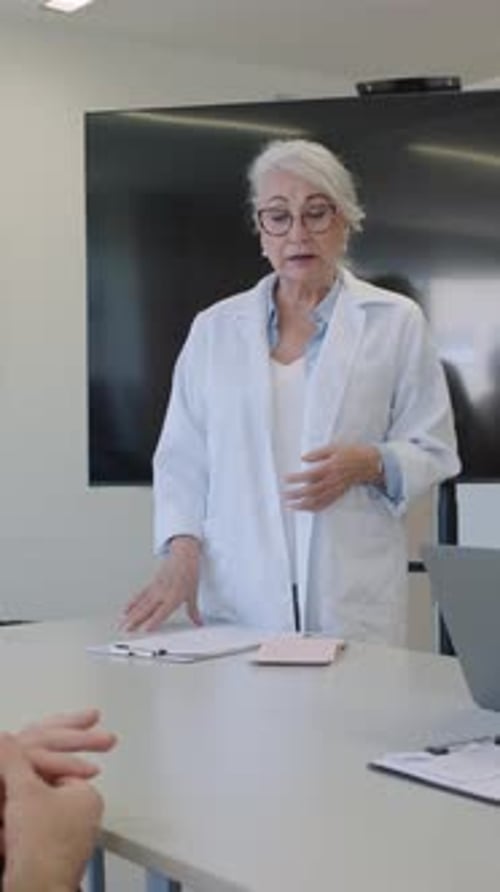 Woman in Lab Coat Speaking at a Table