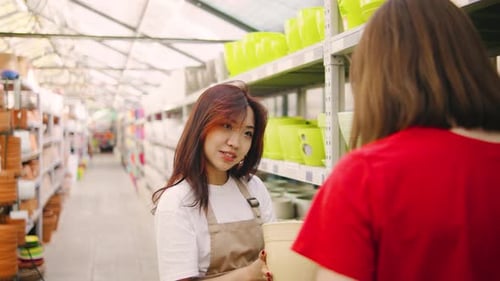 Asian Female Salesperson Advises Buyer Colorful Flowerpots Pots and Various Garden Accessories for