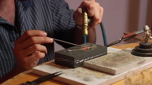 Handwerker verwendet eine Fackel, um in einem Workshop am frühen Abend filigranen Schmuck herzustellen
