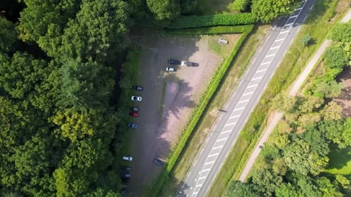 Aerial view of a parking lot beside a multi-lane road with pedestrian paths, surrounded by dense