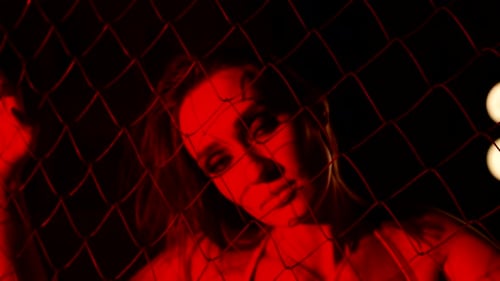 Alluring Woman Poses Behind Fence in Red Light