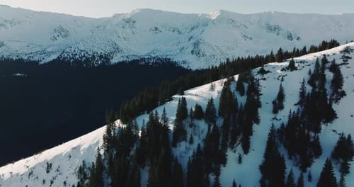 Drone Flies Over Evergreen Forest Rocks Towards Large Snow Covered Mountain Ridge on Cold Winter