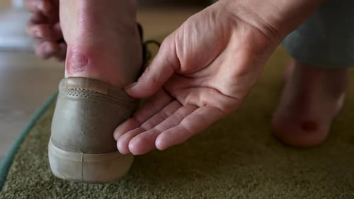 Closeup Back View of Unrecognizable Man Sitting on Bench at Home Takes Off Shoes and Checks Blister