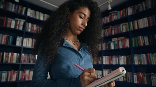 Smart Biracial Female Student Taking Notes for Her Research Paper in Library