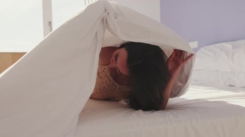 Close-up, happy girl posing in bed. Laughing girl peeps out from under the blankets