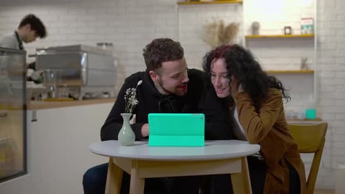Young Couple Smiling, Looking at Tablet in Cafe