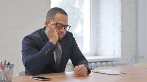 Man Rubbing Eye at Desk in Modern Office