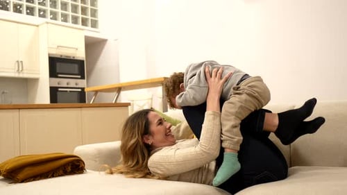 Smiling Woman Lifting Curly Haired Child on Couch