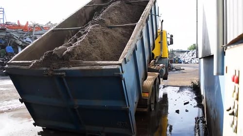 A truck lifts of the ground while loading an overweight container filled with dust,