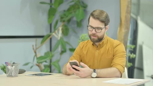 Man Cheering at Desk with Smartphone