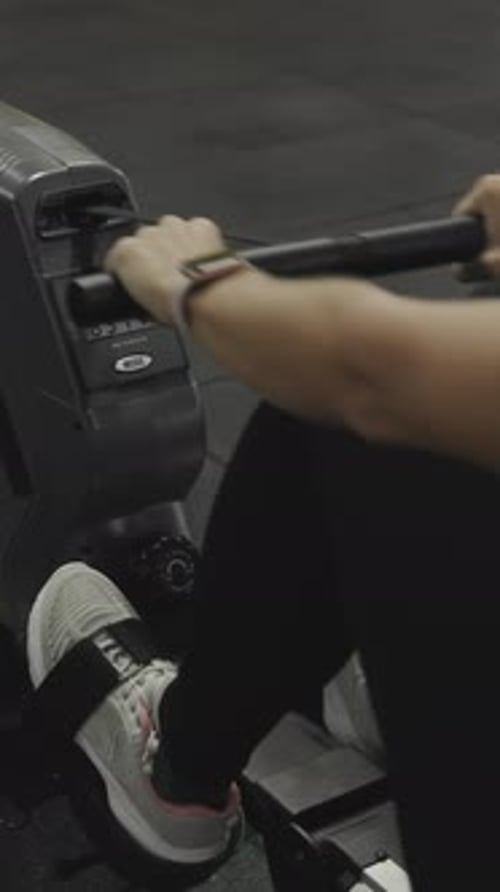 Vertical video. Young woman doing a cardio workout on a rowing machine.