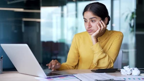 Young bored businesswoman sitting at desk in modern office feeling tired and unmotivated while work