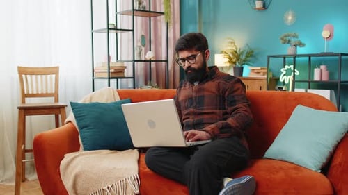 Man Sitting on Couch Opening Laptop Indoors