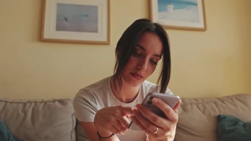 Close up, young woman using mobile phone for texting and scrolling while sitting on sofa at home