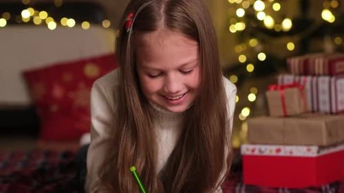 Smiling Kid is Writing Letter to Santa Claus in Room Decorated for Christmas