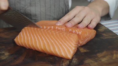 Cutting salmon into three slices on wooden cut board. Close up shot.