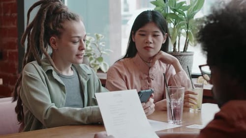 Group of Three Friends Sitting at Restaurant Talking and Looking at Menu