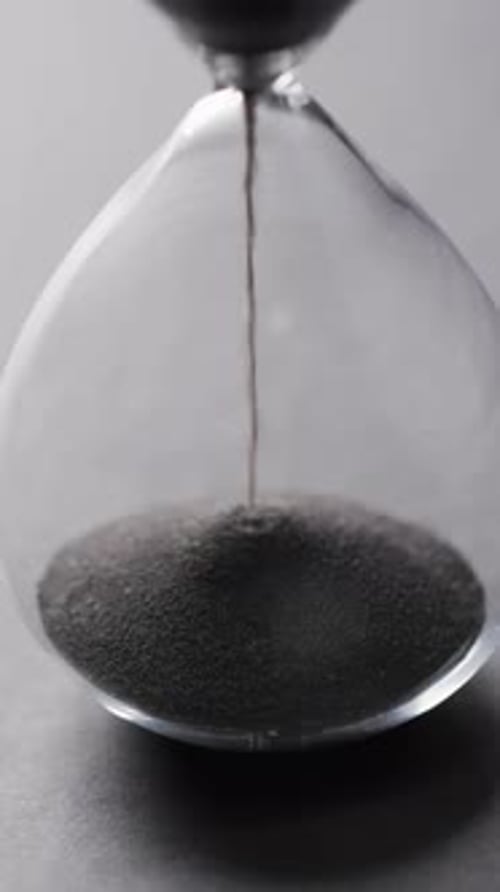 Vertical video of hourglass with sand pouring, copy space on grey background