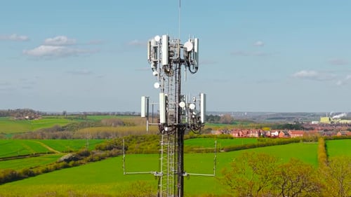 Telecommunication Mast with Antenna Panels Overlooking Farmland and Village Houses in Distance