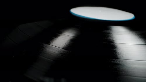 The camera glides from above the vinyl record, revealing its audio grooves. Close-up on a black back