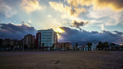 Timelapse with vibrant sunset clouds moving behind buildings near Malaga, Spain