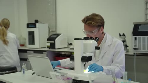 Scientist Using Microscope and Laptop in Laboratory