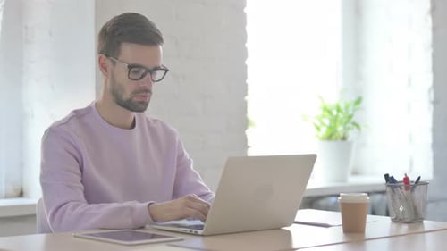 Busy Young Man Typing on Laptop in Office
