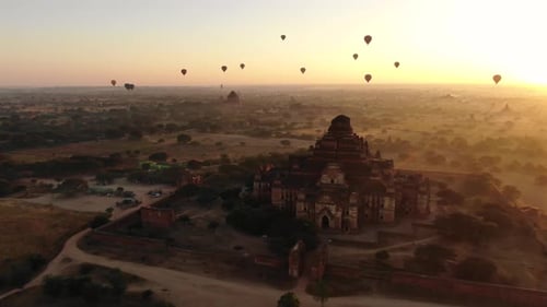 Ancient Buddhist temple in Bagan, Myanmar with dozens of hot air balloons in background during sunri