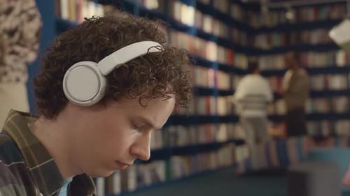 Junger Mann genießt Musik, während er in der Bibliothek studiert