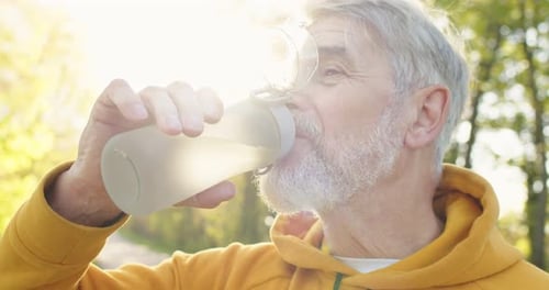 Close Up Portrait of Old Caucasian Handsome Greyhaired Male Standing Outdoors Drinking Water From