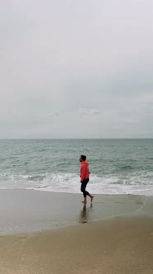 Woman is walking on beach against stormy sea with big waves,. Vertical video