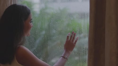 Nahaufnahme einer Frau, die während der Regenzeit am Fenster posiert Nahaufnahme einer jungen Frau, die sich berührt