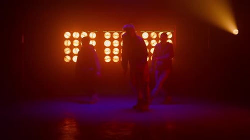 Three young men dancing in a studio with lights