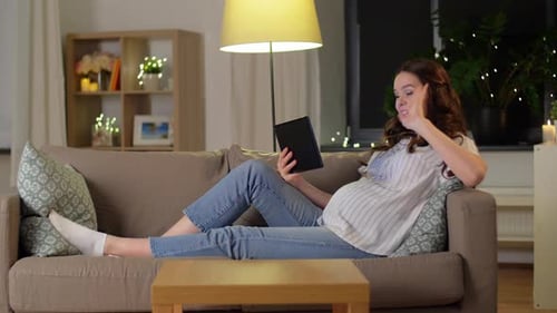 Pregnant woman using tablet, relaxing on living room sofa