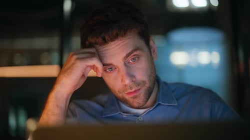 Gros plan : un manager fatigué regarde un ordinateur portable dans un bureau sombre, travailleur indépendant surmené