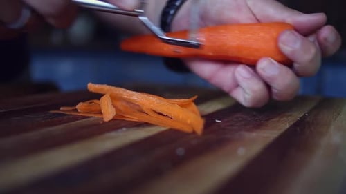 Man Peels Carrot with Peeler on Cutting Board