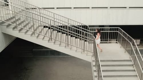 Beautiful girl in a white dress climbs the stairs. Attractive girl walking