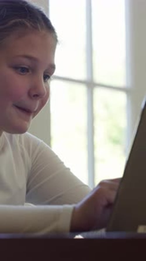 Smiling Girl Uses Tablet at Home During Day