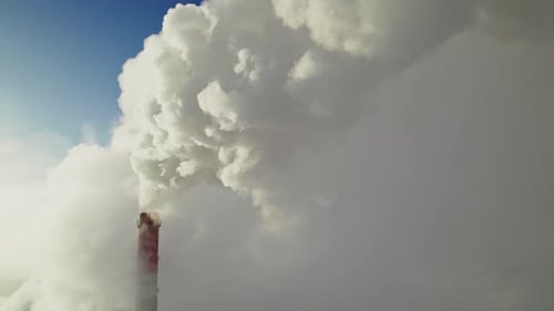 Factory chimney spewing white smoke against blue sky